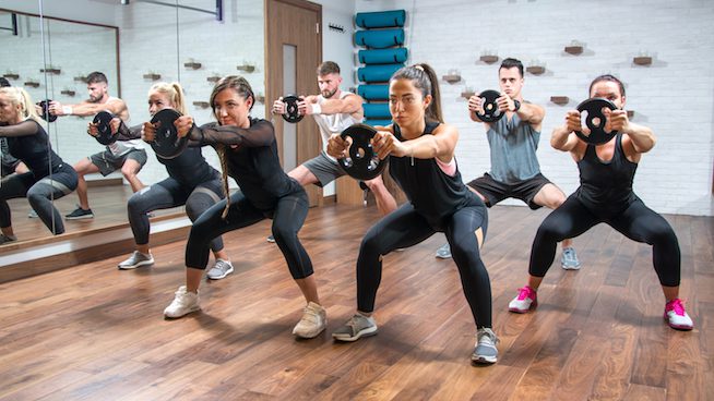 Group of sporty women and men exercising together with weight plates in health club.